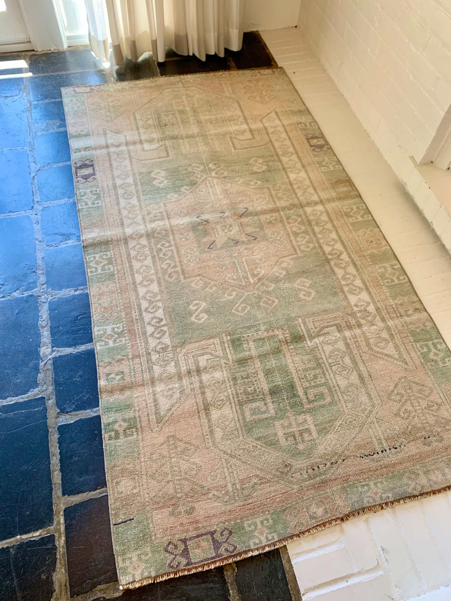 3’7”x6’7” beige and green Oushak area rug on tiled floor.