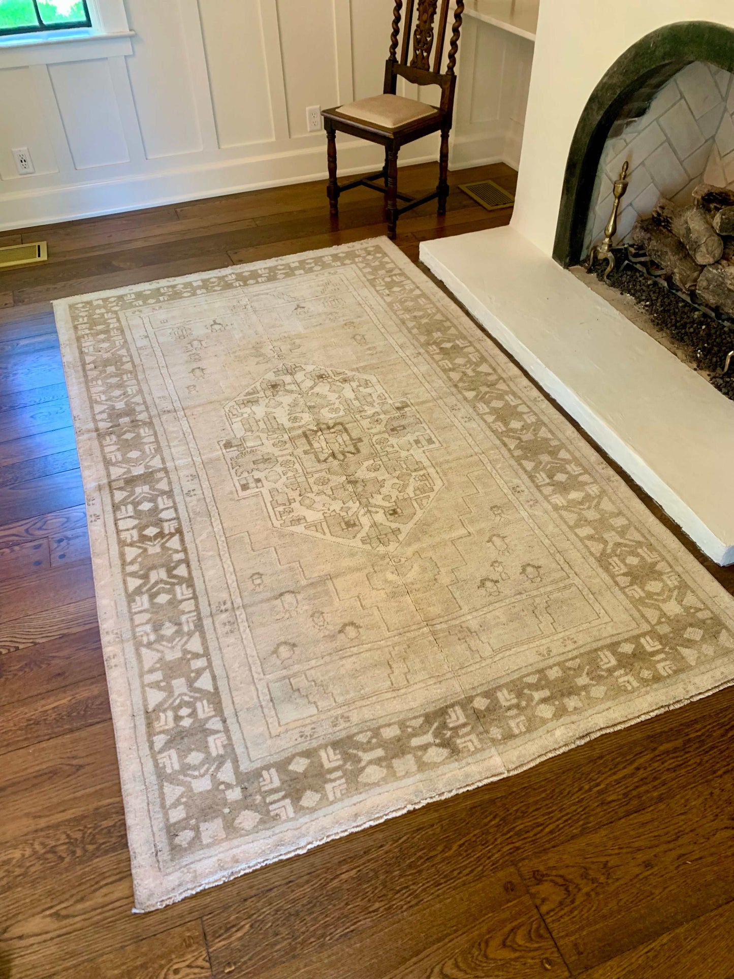 5’1”x8’6” muted vintage Oushak area rug in light beige, cream, and brown on wooden floor near fireplace