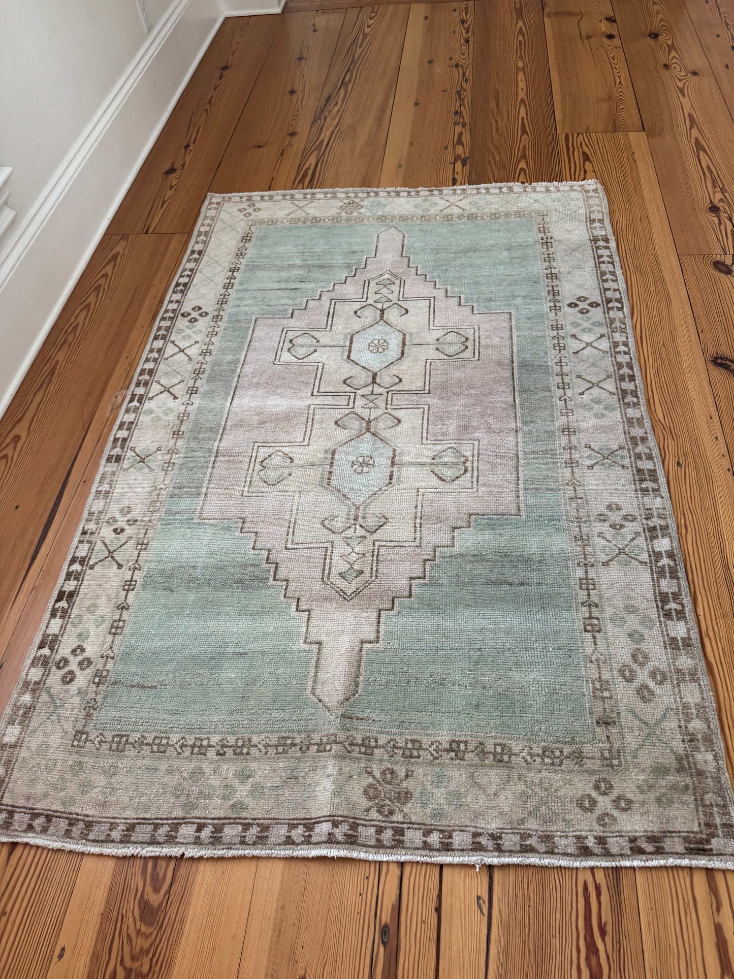 4’2”x6’4” vintage Oushak area rug with aqua, lavender, cream, and brown geometric design on hardwood floor