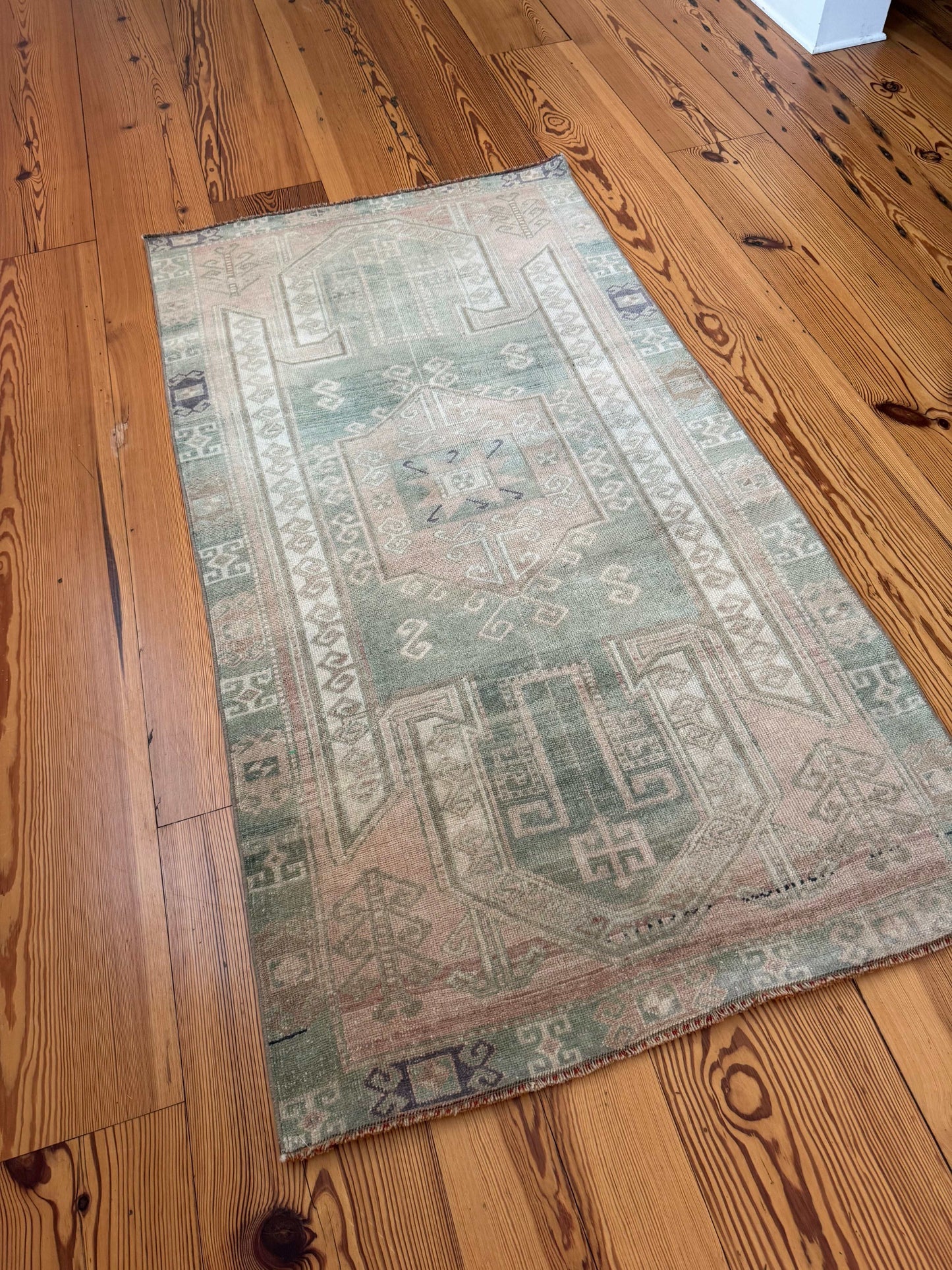 3’7”x6’7” vintage Oushak area rug in beige, green, and purple tones on wooden floor
