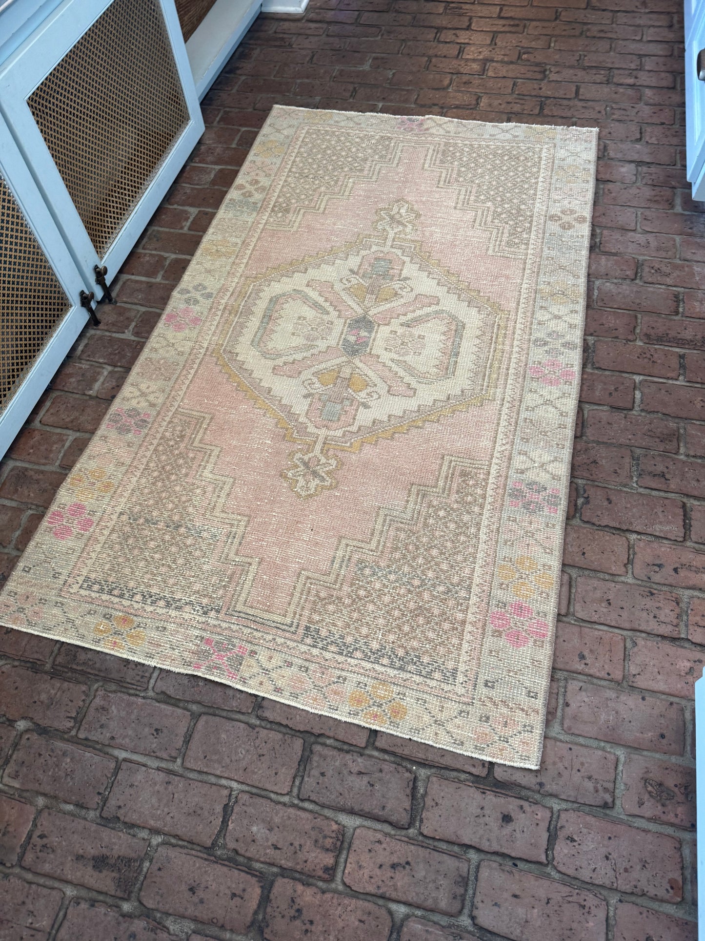 3'5" x 6' area rug with blush pink, brown, and blue geometric patterns on brick floor