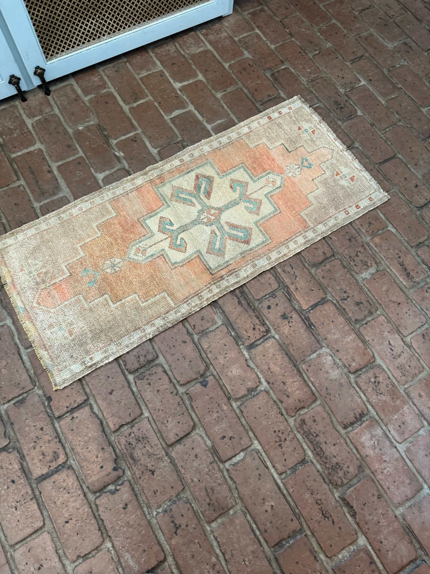 Small Turkish Oushak rug with orange, green, and brown design on brick floor.