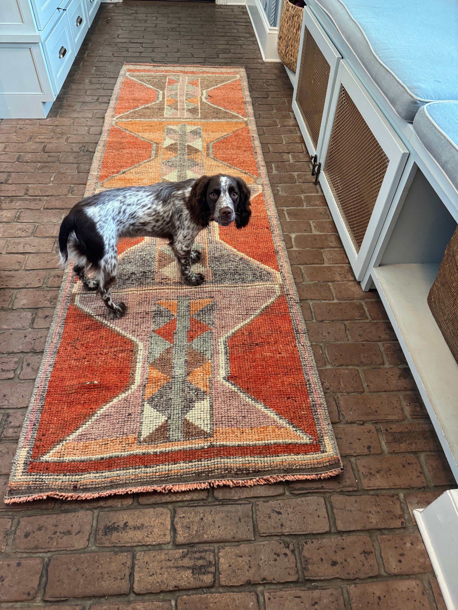 3' x 10'1" rug runner with bold orange and gray geometric patterns on brick floor
