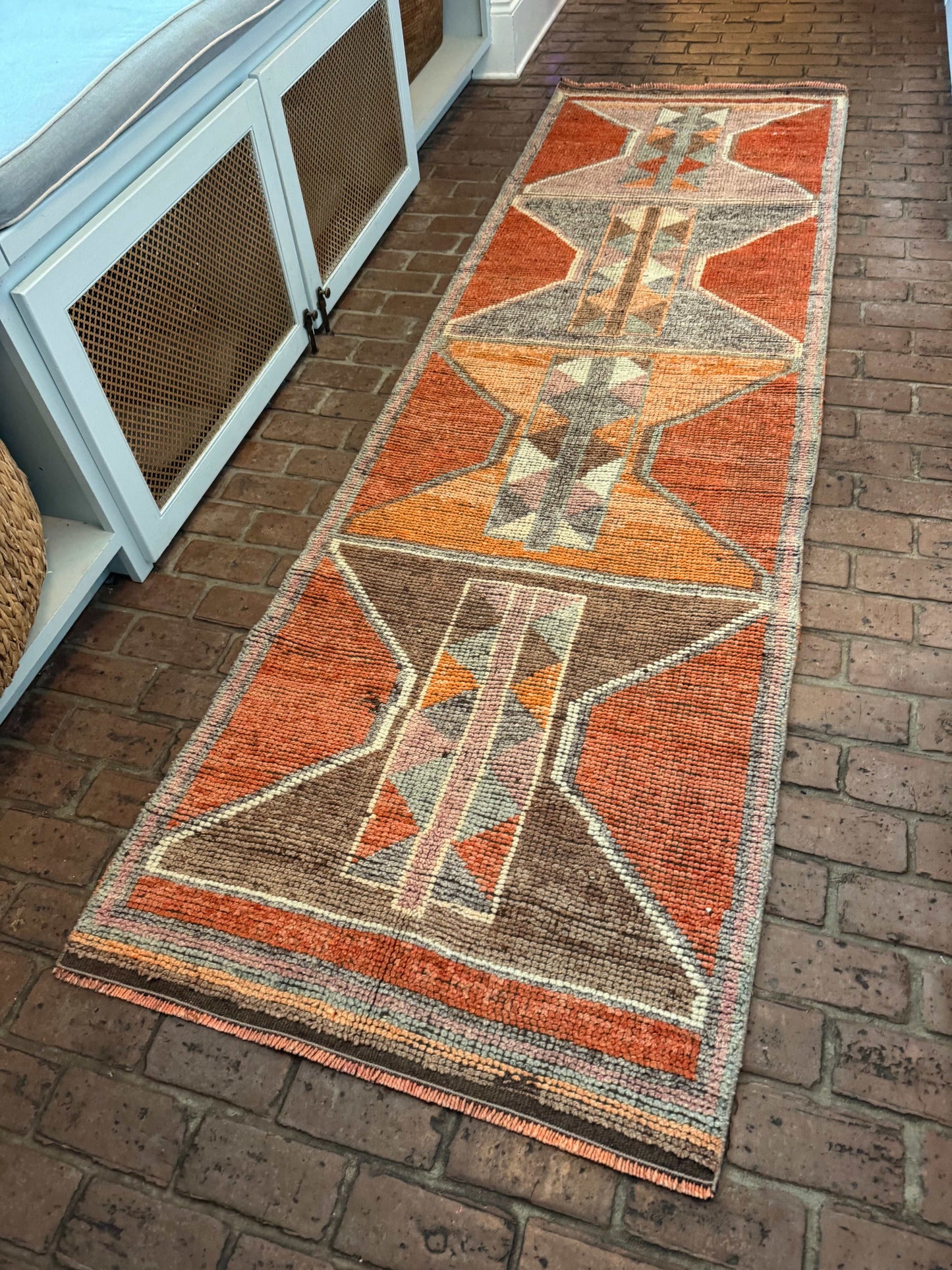 3' x 10'1" rug runner with bold orange and gray geometric patterns on brick floor