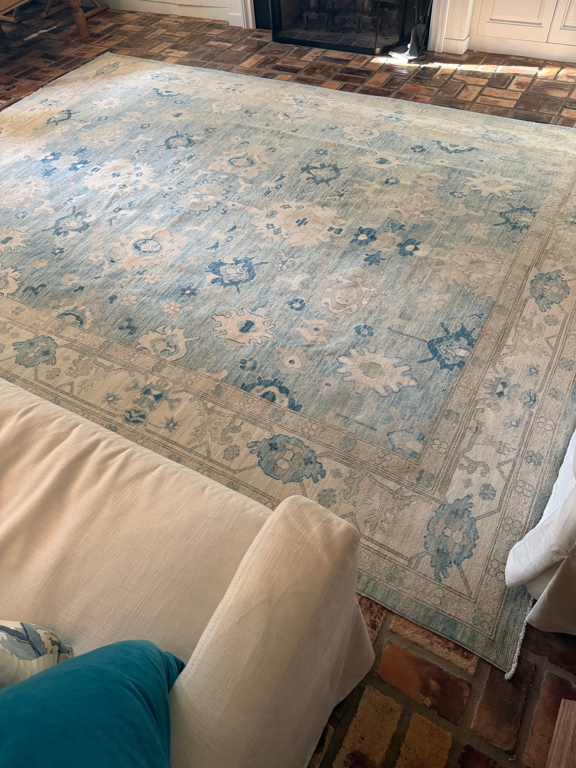 Person rolling out a large floral-patterned rug on a wooden floor.