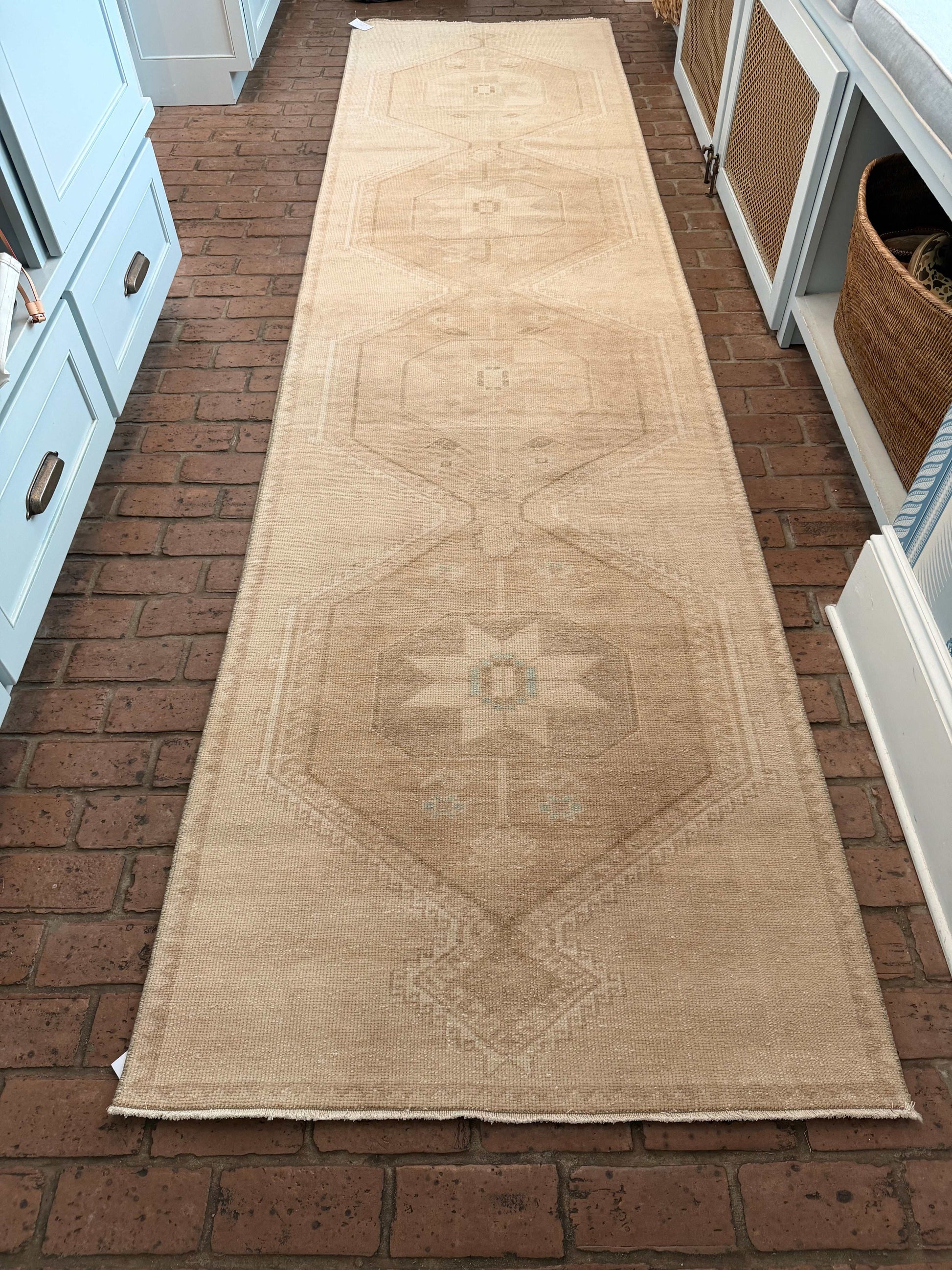 Large beige rug with geometric pattern hanging on a brick wall.