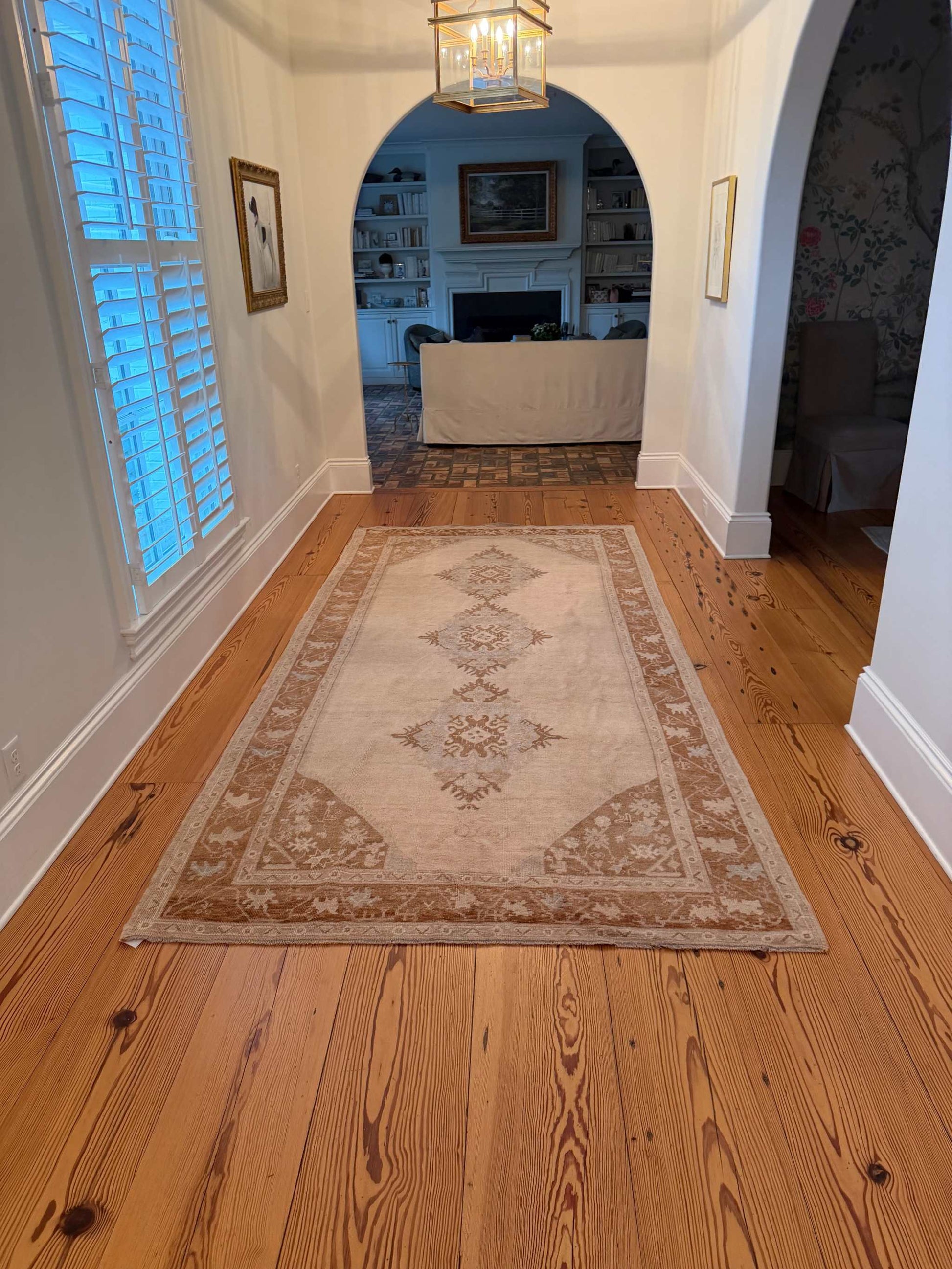 Decorative rug on a wooden floor with a ceiling light fixture and wall art in the background.
